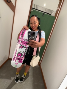 Indigo is holding a hello kitty design GIRL skateboard standing in a change room taking a 'selfie'